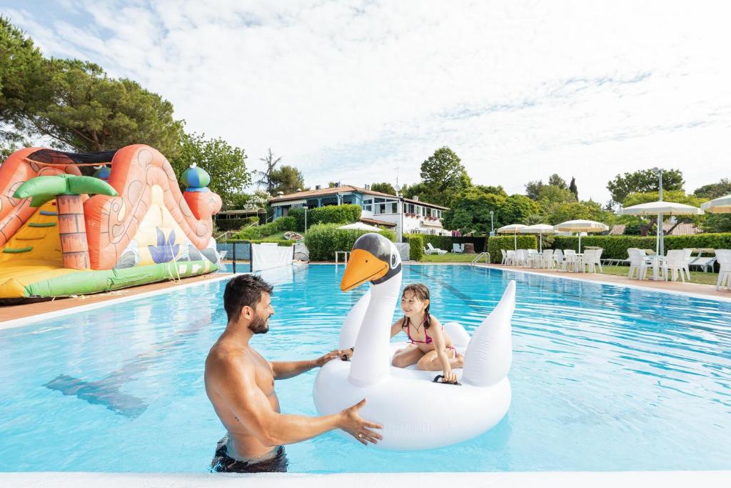 Ein Mann und ein Mädchen reiten auf einem aufblasbaren Schwan im Schwimmbad in der Unterkunft Appartamento cod. 456 Taunus Vacanze in Marcelli