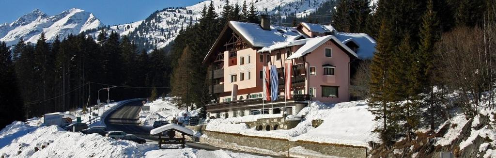 ein Haus auf einem schneebedeckten Hügel mit einem Berg in der Unterkunft Hotel Mooserkreuz in Sankt Anton am Arlberg