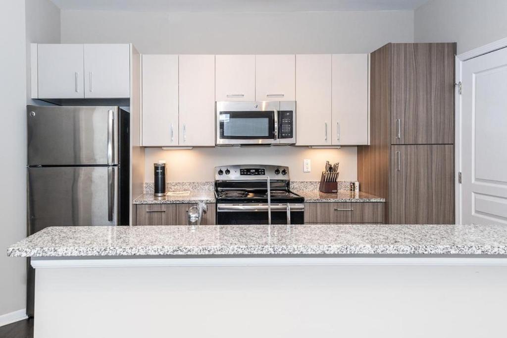 una cucina con armadi bianchi e frigorifero in acciaio inossidabile di Landing - Modern Apartment with Amazing Amenities (ID4378) ad Auburn Hills