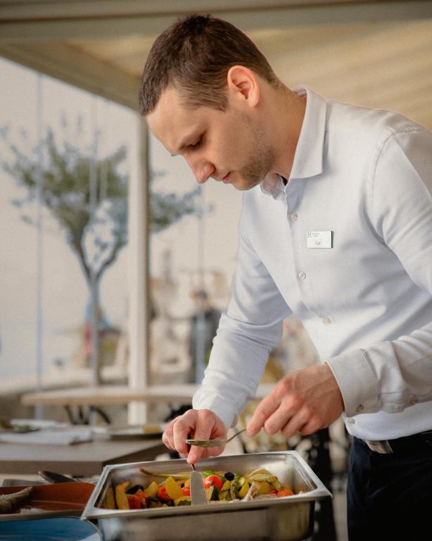 a man in a kitchen preparing food in a pan at Hotel Piran in Piran