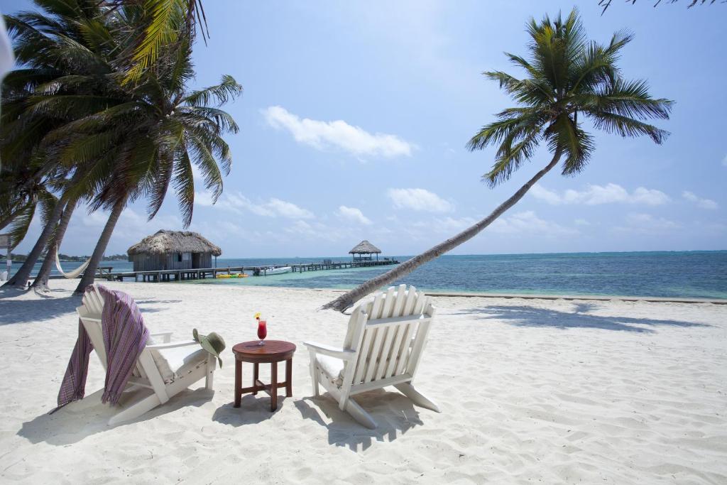 two chairs and a table on a beach with palm trees at Victoria House Resort & Spa in San Pedro