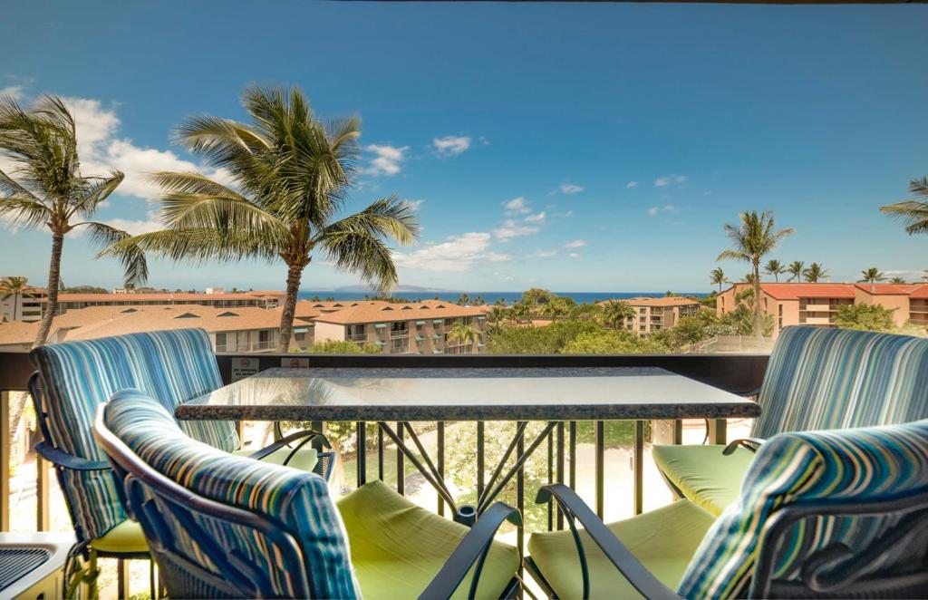 balcón con sillas, mesa y palmeras en Maui Vista 3406 - Ocean View Penthouse Sleeps 7, en Kihei