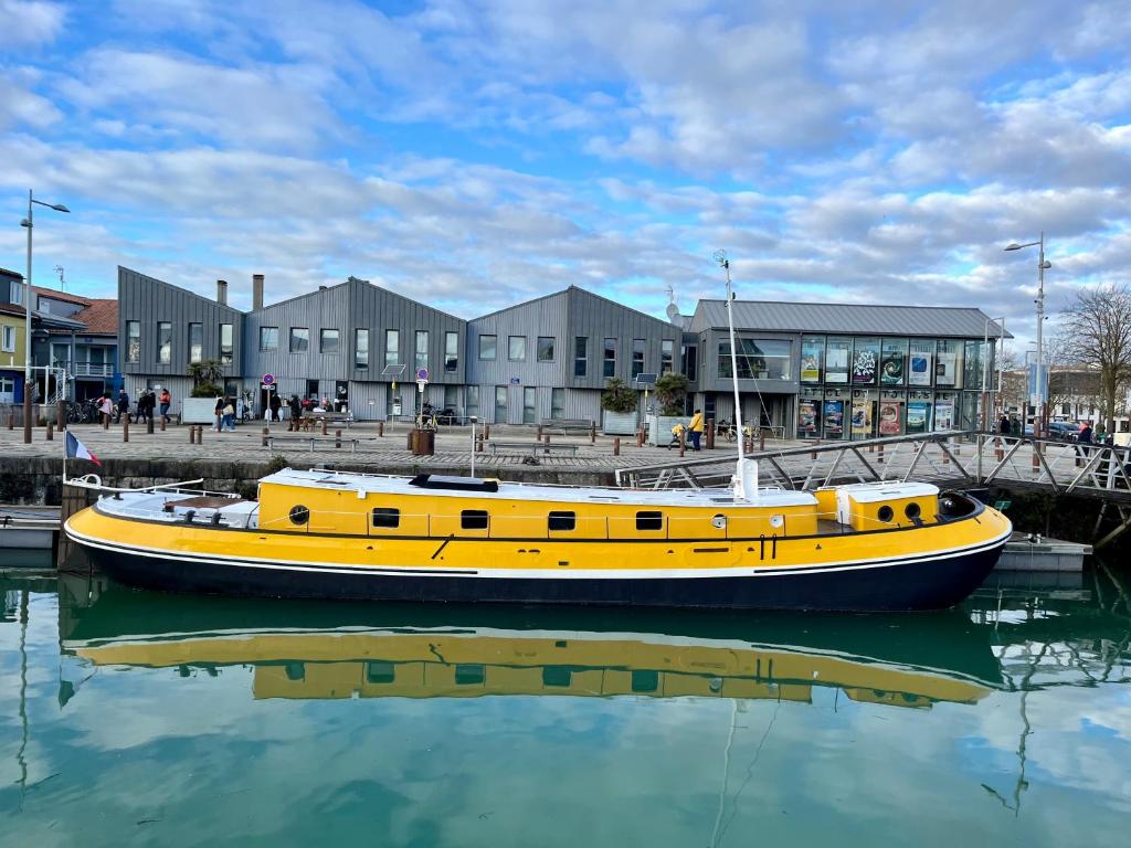 un bateau jaune assis dans l'eau devant un bâtiment dans l'établissement UNE PENICHE DANS LE BASSIN À FLOT DU VIEUX PORT, à La Rochelle