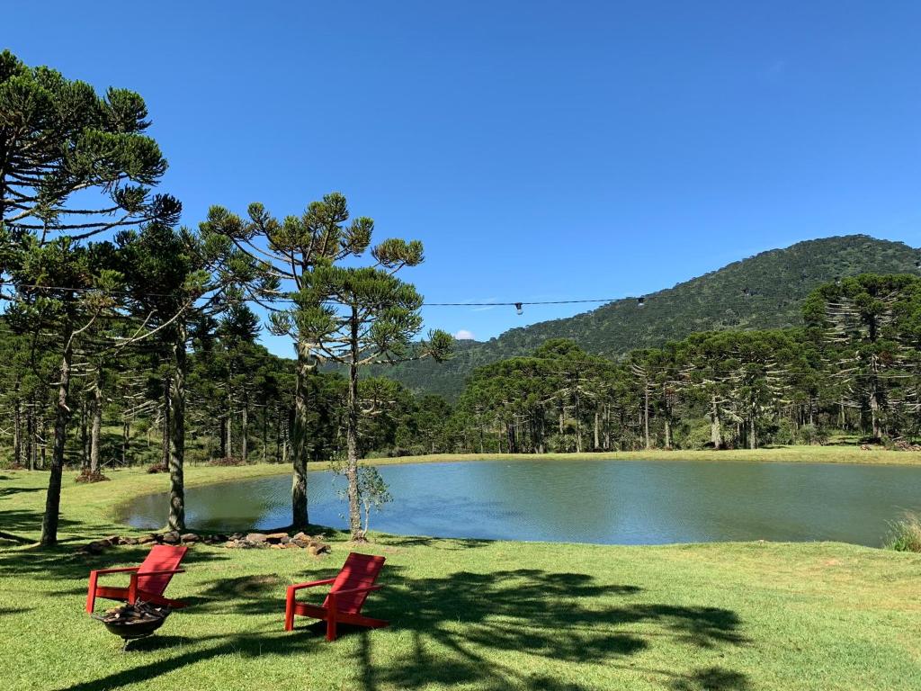 two red chairs sitting in front of a lake at Estalagem Santa Clara in Urubici