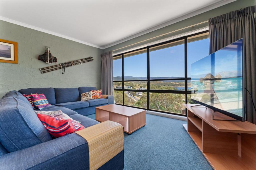 a living room with a blue couch and a large window at Alpine Mountain View 18 - 4BR l Mountain Views l Swimming Pool l Air-Con l WiFi in Jindabyne