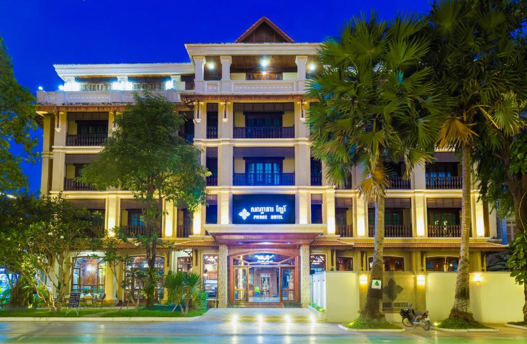un grand bâtiment avec des palmiers devant lui dans l'établissement Pierre Hotel, à Siem Reap