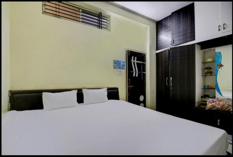 a bedroom with a white bed and a black cabinet at HOTEL SATYAM SHREE in Indore