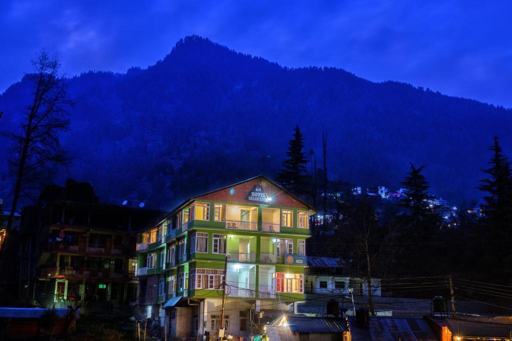 un edificio con luces encendidas frente a una montaña en HOTEL DREAM RIVER BY ARH HOTELS, en Manali