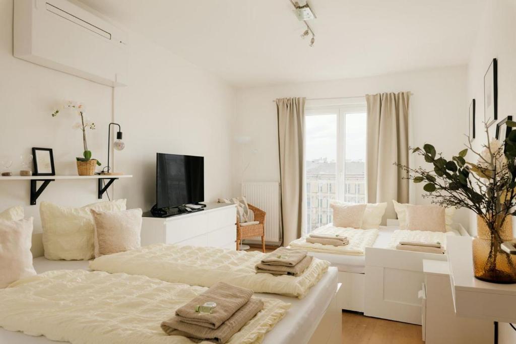 a white bedroom with two beds and a tv at Apartment ZENTRAL direkt an U-BAHN STATION in Vienna