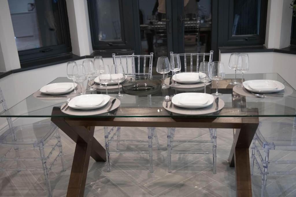 a glass table with chairs and plates and wine glasses at Luxury Kingsize Room in London in Catford