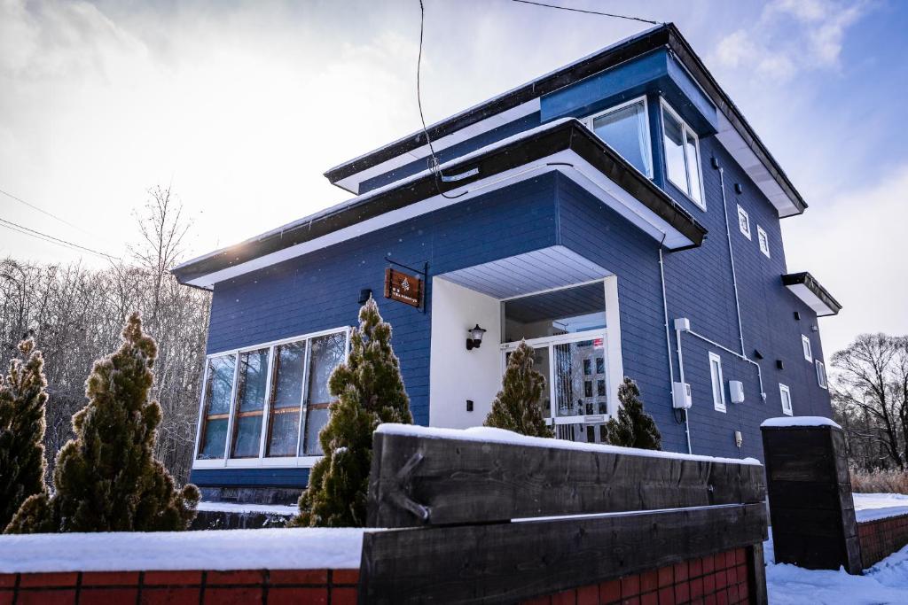 una casa azul con nieve delante en ヴィラYukara緑屋, en Nanae