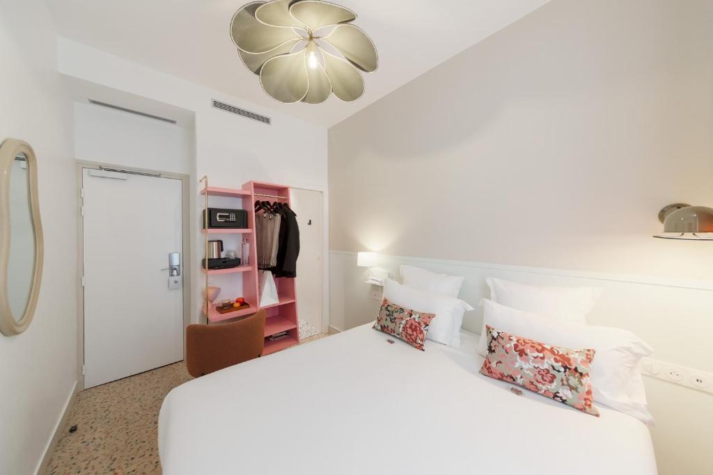 a white bedroom with a large white bed with pillows at Trendy Canettes Hotel in Paris