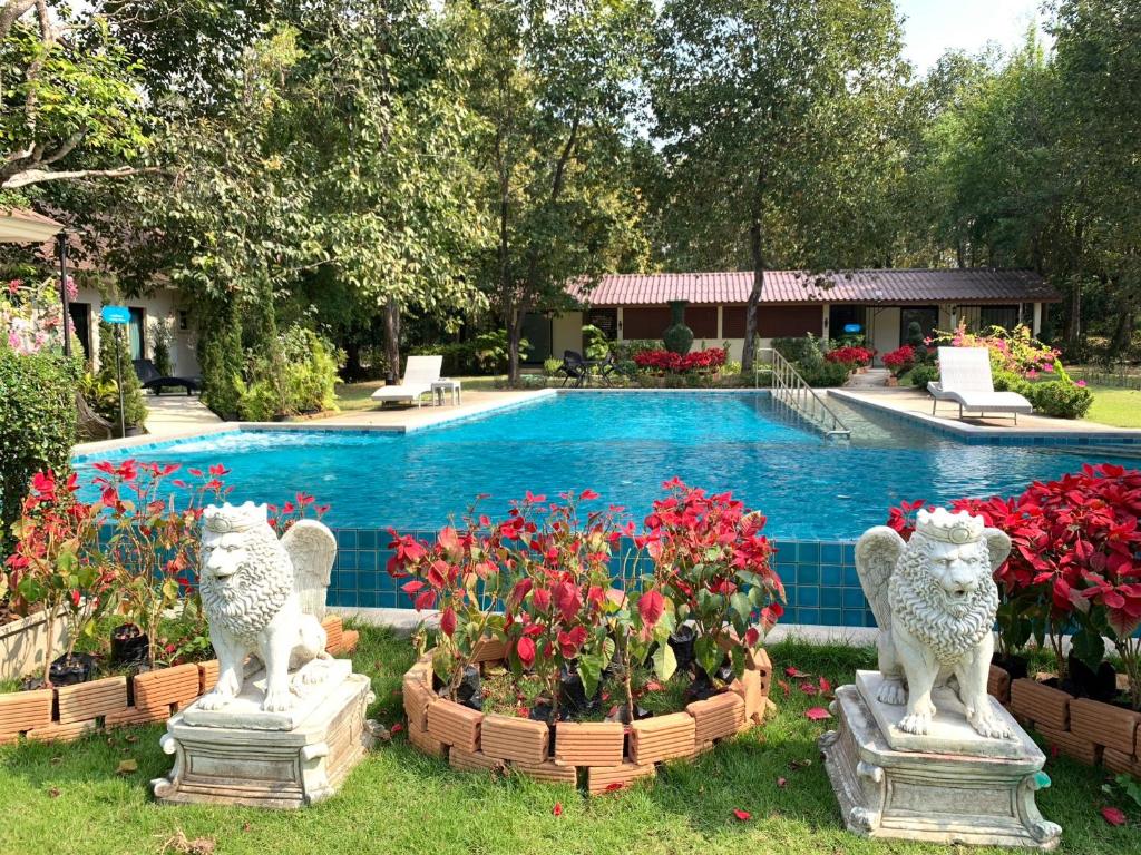 una piscina con dos estatuas de leones y flores en Baan Pingkan Wellness Resort en San Kamphaeng