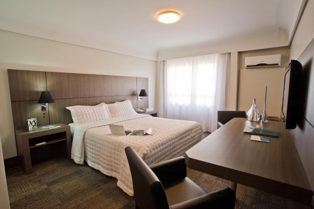 a hotel room with a large bed and a desk at Slaviero Curitiba Centro in Curitiba