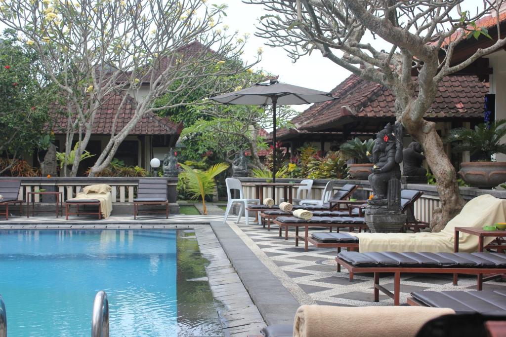 a pool with chairs and tables and an umbrella at Sagitarius Inn in Ubud
