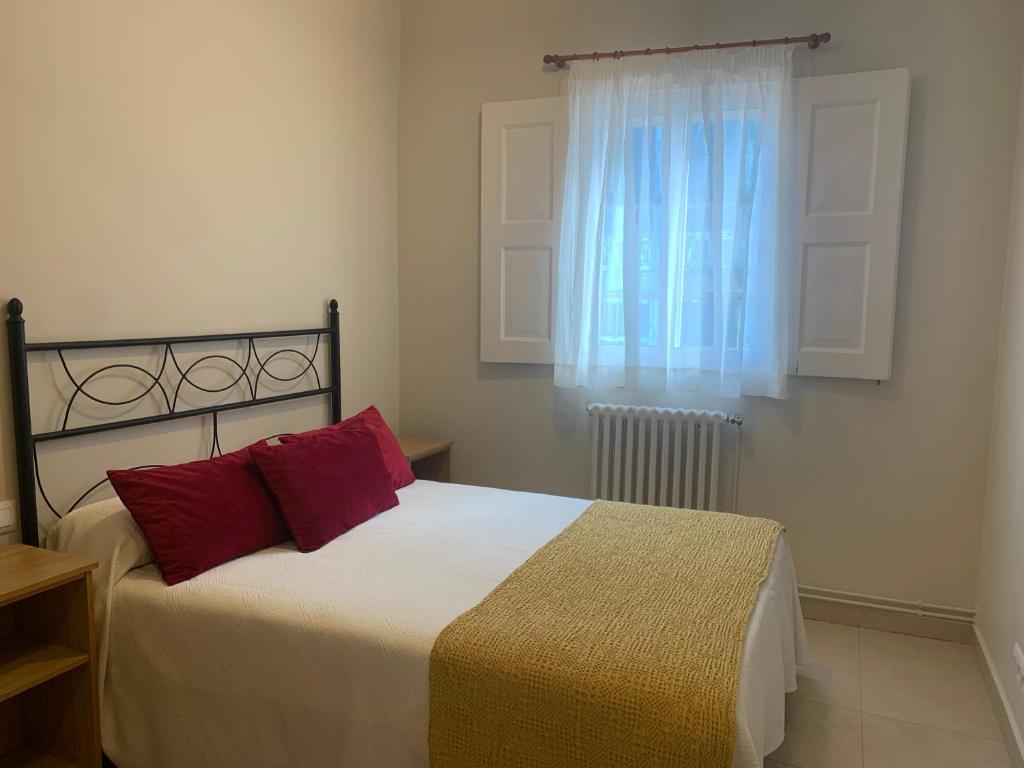 Un dormitorio con una cama con almohadas rojas y una ventana en Hospedaje Ramos, en Santiago de Compostela