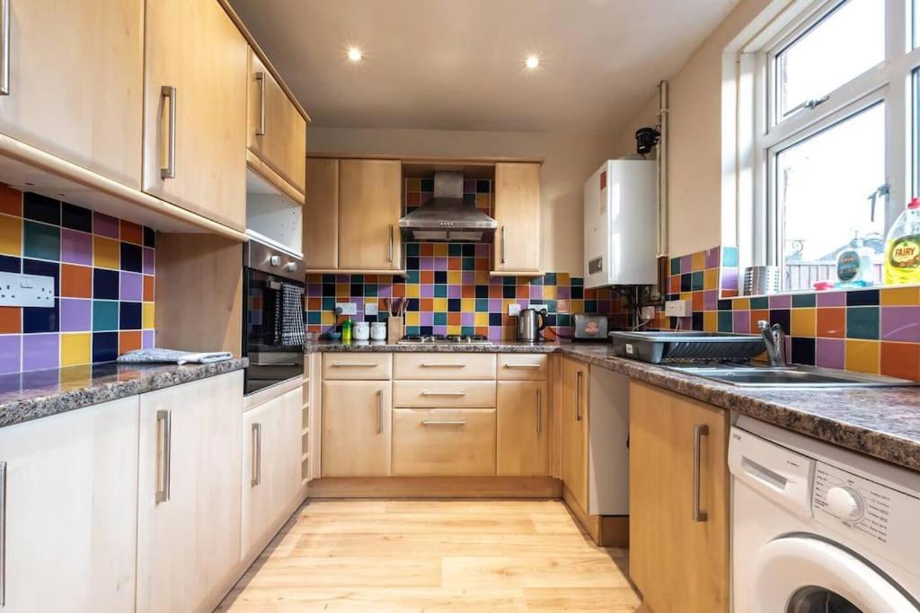 una cocina con armarios de madera y azulejos coloridos en la pared en Bluebell House en Southampton