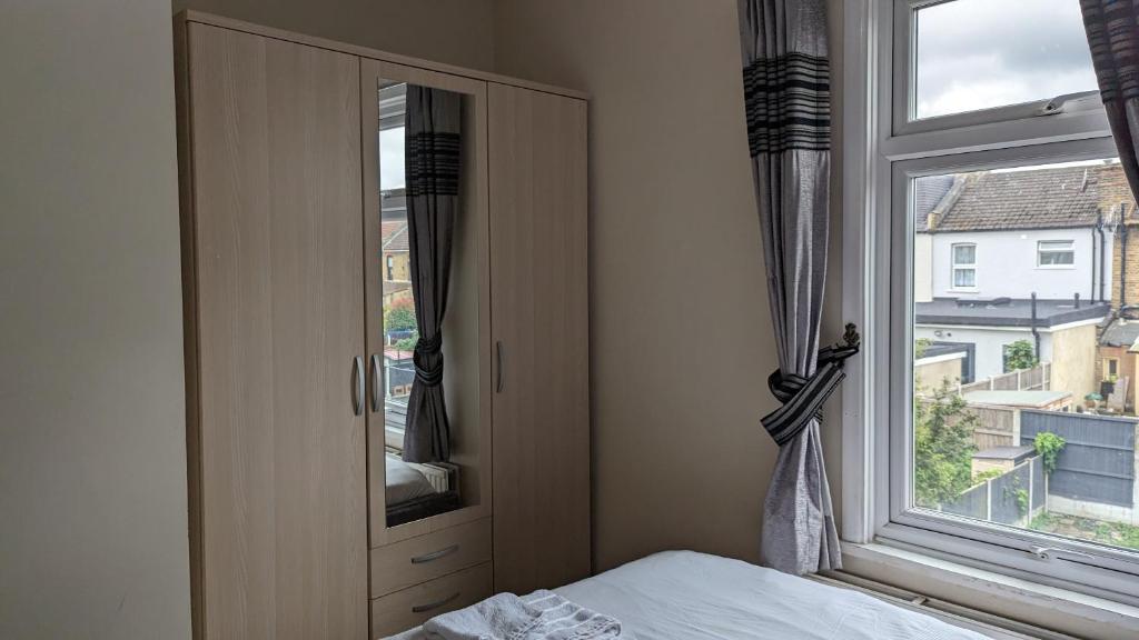 1 dormitorio con ventana, 1 cama y vestidor en 3 bedroom house,4beds, 2 baths Ilford ,12 mins to Stratford en Londres