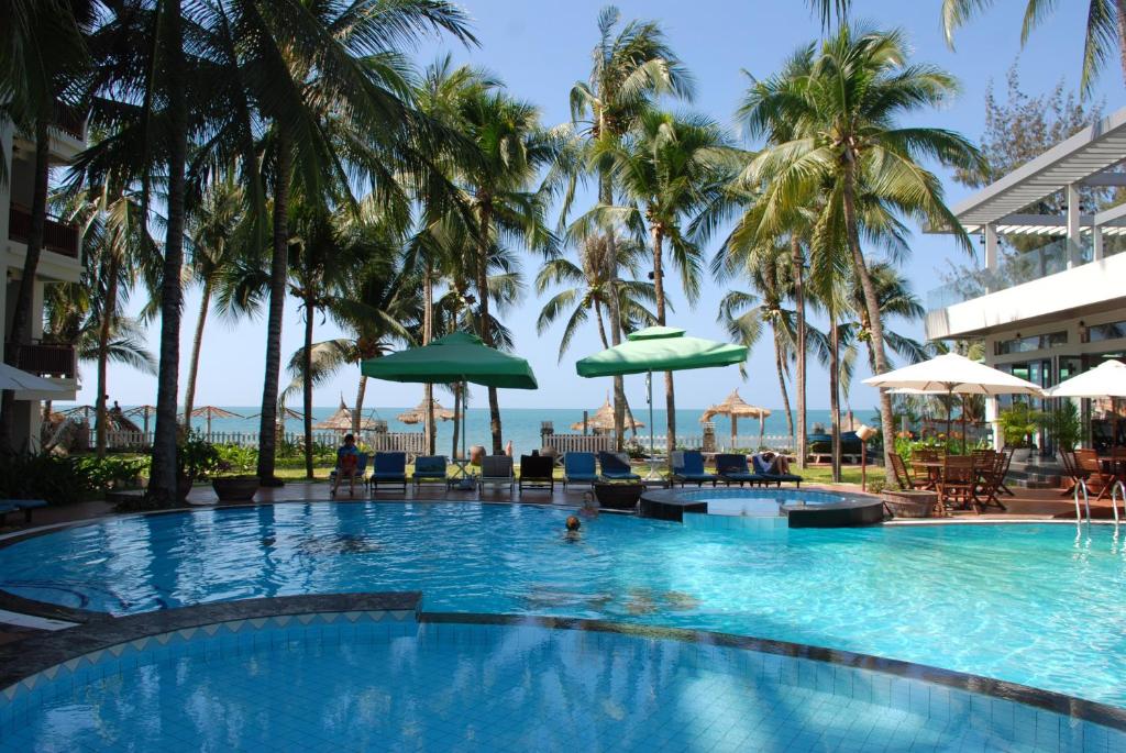 a swimming pool with palm trees and the ocean in the background at Canary Beach Resort in Mui Ne