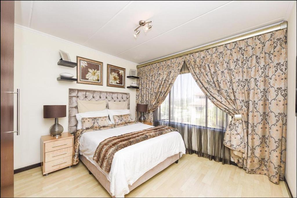 1 dormitorio con 1 cama y una ventana con cortinas en The Kanyin, en Sandton