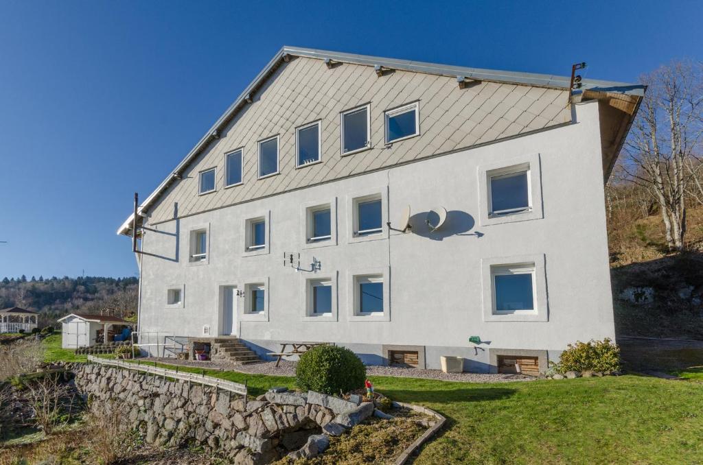 - un grand bâtiment blanc avec un mur en pierre dans l'établissement PARME Appt spacieux et calme plein sud, vue panoramique, à La Bresse