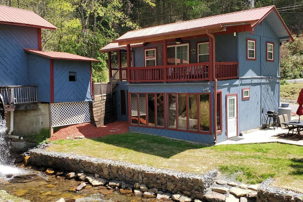 een groot blauw huis met een terras en een vijver bij Waterwheel Cabin by the Creek in Murphy