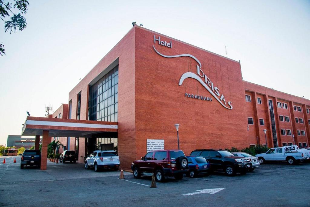 ein großes rotes Backsteingebäude mit Autos auf einem Parkplatz in der Unterkunft HOTEL BRISAS PARAGUANÁ in Punto Fijo