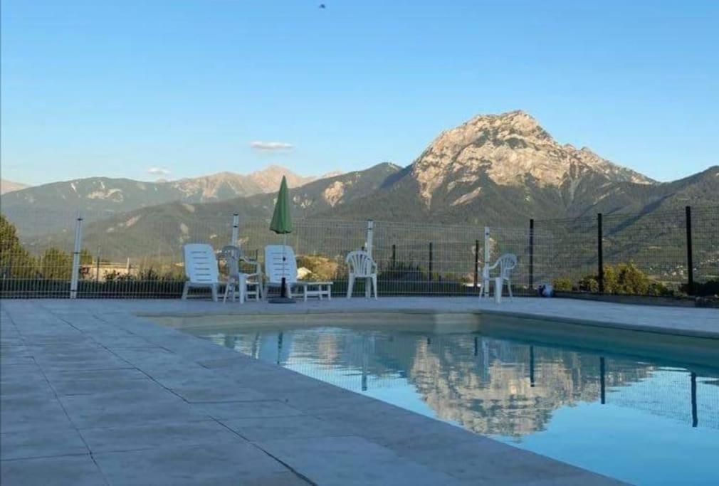 une piscine avec des chaises et des montagnes en arrière-plan dans l'établissement Entre Lac et Montagne - Piscine & Tennis, à Prunières