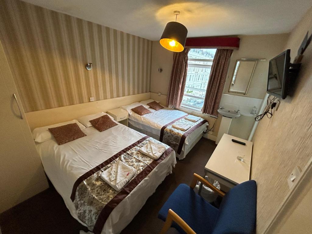 um quarto de hotel com duas camas e uma cadeira em Earls Court Hotel em Londres