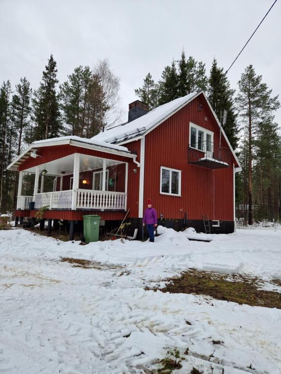 Jock的住宿－Överkalix Kalixalven Lodge Jockfall，站在雪中红房子前面的人