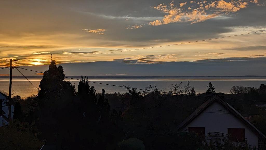 una puesta de sol sobre el agua con una casa en primer plano en Gabi háza en Balatonalmádi