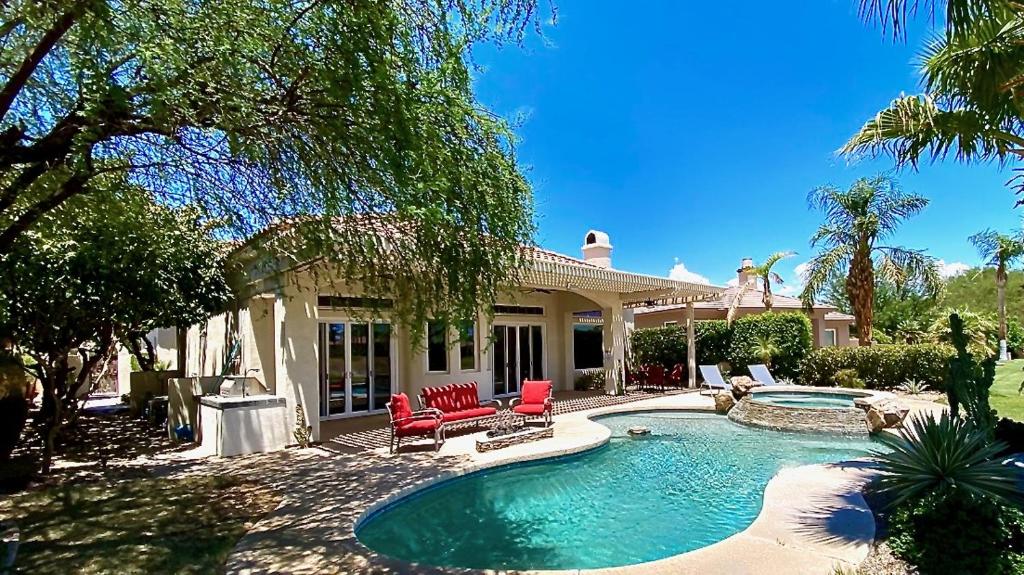 a house with a swimming pool and two red chairs at TEE TIME: 2 bed + convertible den; private pool and spa, VIEWS! A Greenday property. in Rancho Mirage