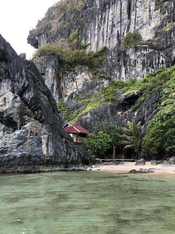 a house on a beach next to a mountain at Just Inn2 beachfront in El Nido