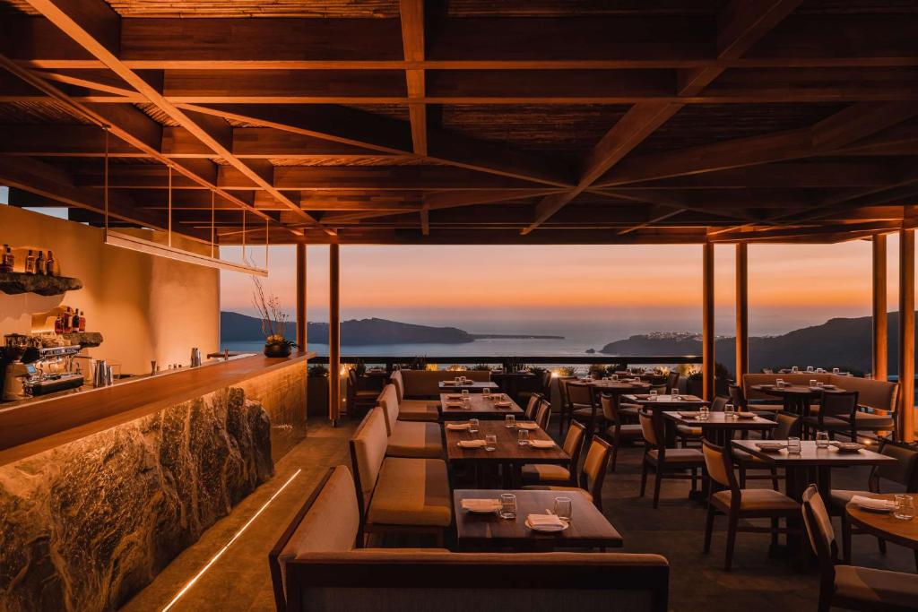 a restaurant with tables and chairs with the sunset in the background at Nobu Hotel Santorini in Imerovigli