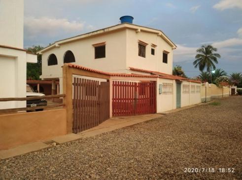 una casa bianca con un cancello rosso e un vialetto di Tú Casa de playa La Milagrosa a Boca de Uchire