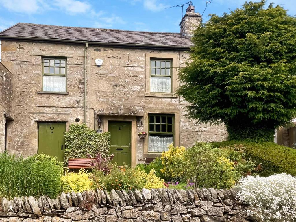 an old stone house with green doors and a tree at Spoutscroft Cottage in Austwick