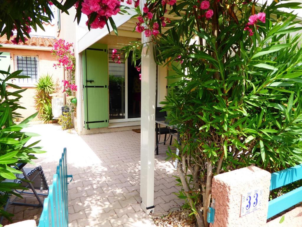 une maison avec une porte verte et un arbre avec des fleurs roses dans l'établissement Pavillon climatisé 4/5 pers, grande terrasse, proche plage et commerces, parking sécurisé - FR-1-776-6, à Argelès-sur-Mer
