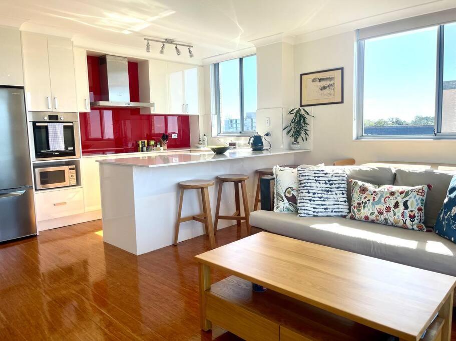 a living room with a couch and a kitchen at Perfect Randwick Escape -2Bdrm-Parking - Walk To Hospital & Shops in Sydney