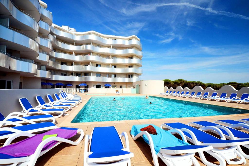 a swimming pool with lounge chairs and a building at Résidence Odalys Le Lotus Blanc in Le Barcarès