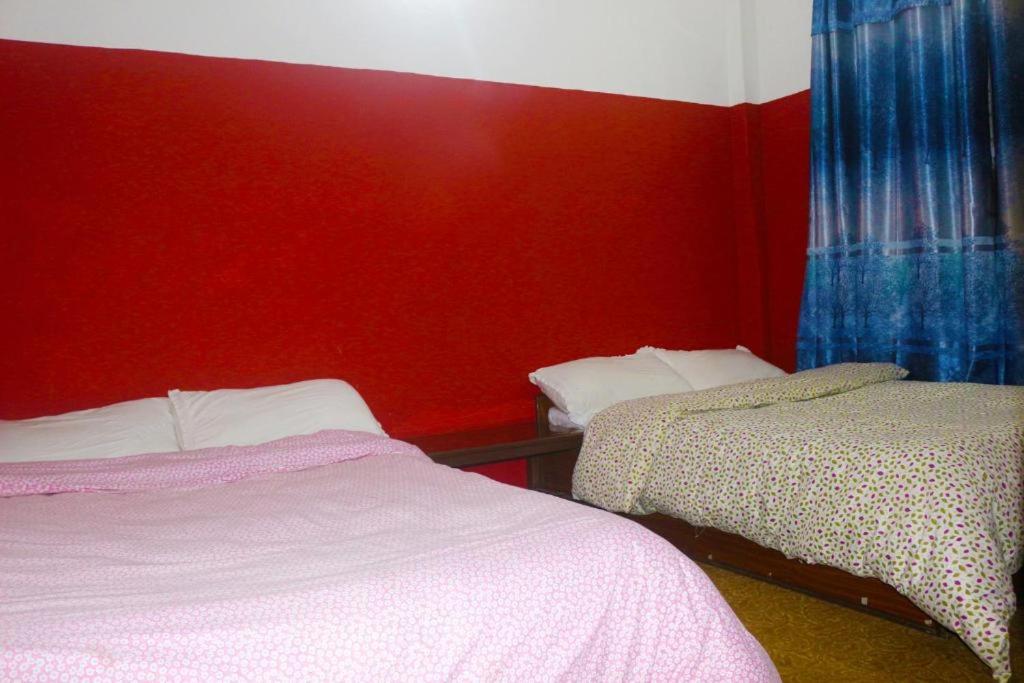 um quarto com 2 camas e uma parede vermelha em Yours Family Restaurant and Homestay em Deorāli