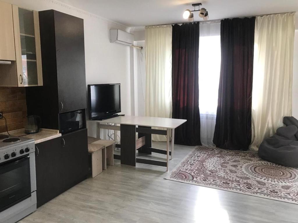 uma cozinha com uma mesa e uma televisão num quarto em Квартира em Almaty
