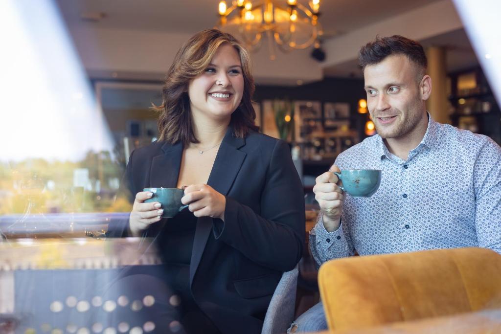 Ein Mann und eine Frau sitzen am Tisch und trinken Kaffee. in der Unterkunft Mercure Hotel Bad Oeynhausen City in Bad Oeynhausen