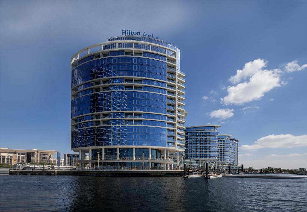 Hilton Dubai Creek Hotel & Residences في دبي: مبنى أزرق طويل بجوار جسم من الماء