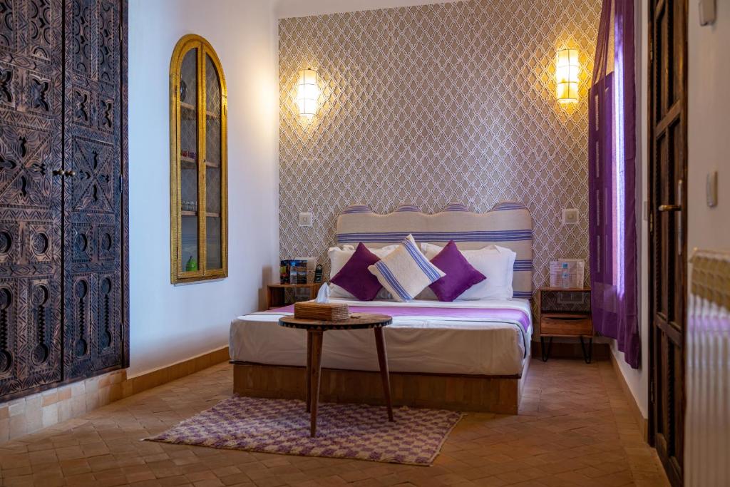 Un dormitorio con una cama con paredes moradas y una mesa. en Riad Cologne & Spa, en Marrakech