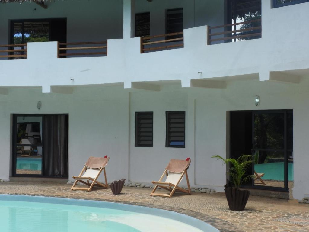 two chairs sitting in front of a building with a swimming pool at Auberge SAKATI'Art in Nosy Be