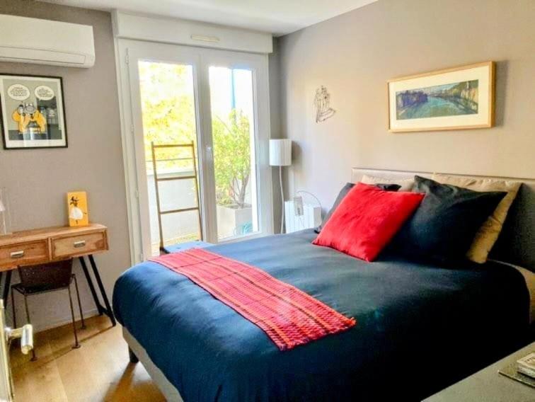 Un dormitorio con una cama azul con almohadas rojas y un escritorio. en Junior suite avec balcon, en Lyon