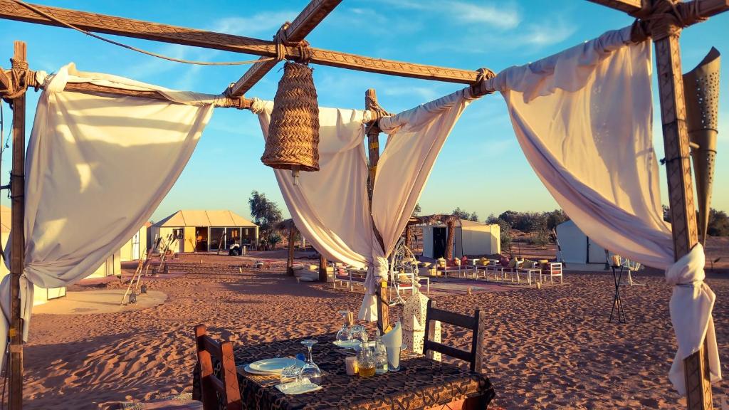 a table in the middle of a desert with white curtains at Horaz luxury camp in Merzouga