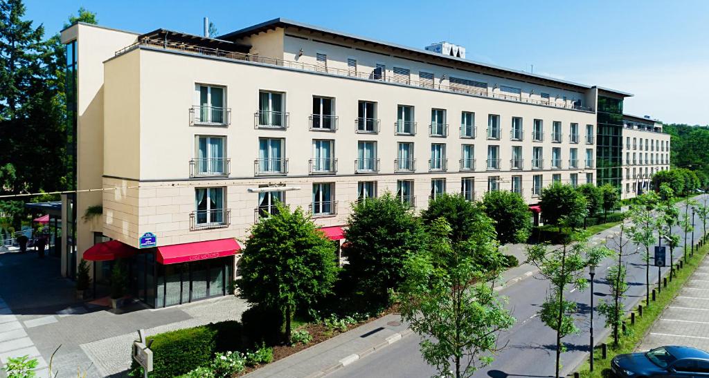 - un grand bâtiment blanc dans une rue de la ville bordée d'arbres dans l'établissement Victor's Residenz-Hotel Saarbrücken, à Sarrebruck