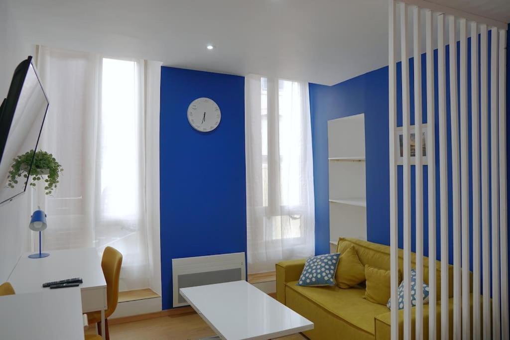un salon avec un canapé et une horloge sur un mur bleu dans l'établissement Le Majorelle-centre ville-accès 24h- parking free, à Montluçon