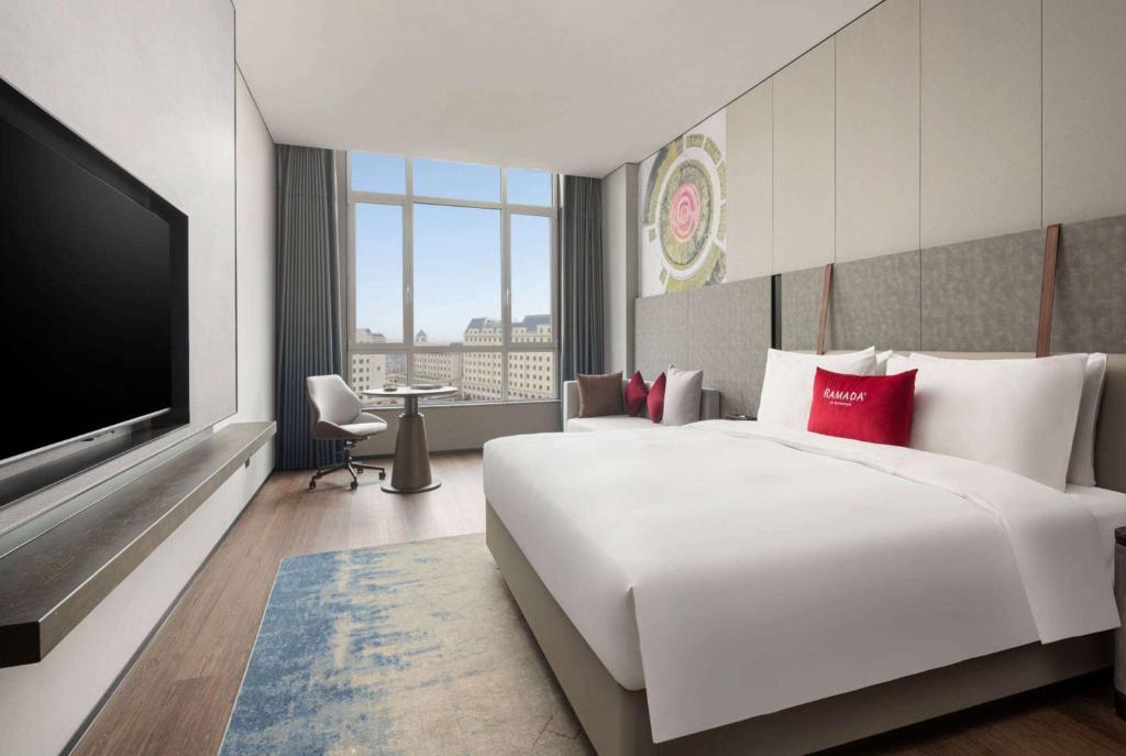 a hotel room with a large bed and a flat screen tv at Ramada by Wyndham Qingdao Jiaodong International Airport in Qingdao